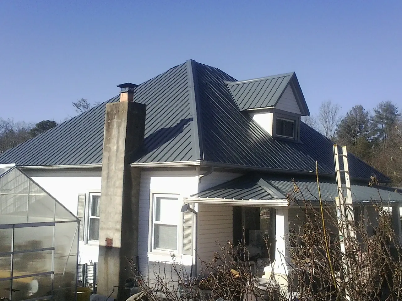 Dark blue standing seam metal roof on a white farmhouse with dormer — Slate & Tile Roof Repair by Roofing Brothers in Echo