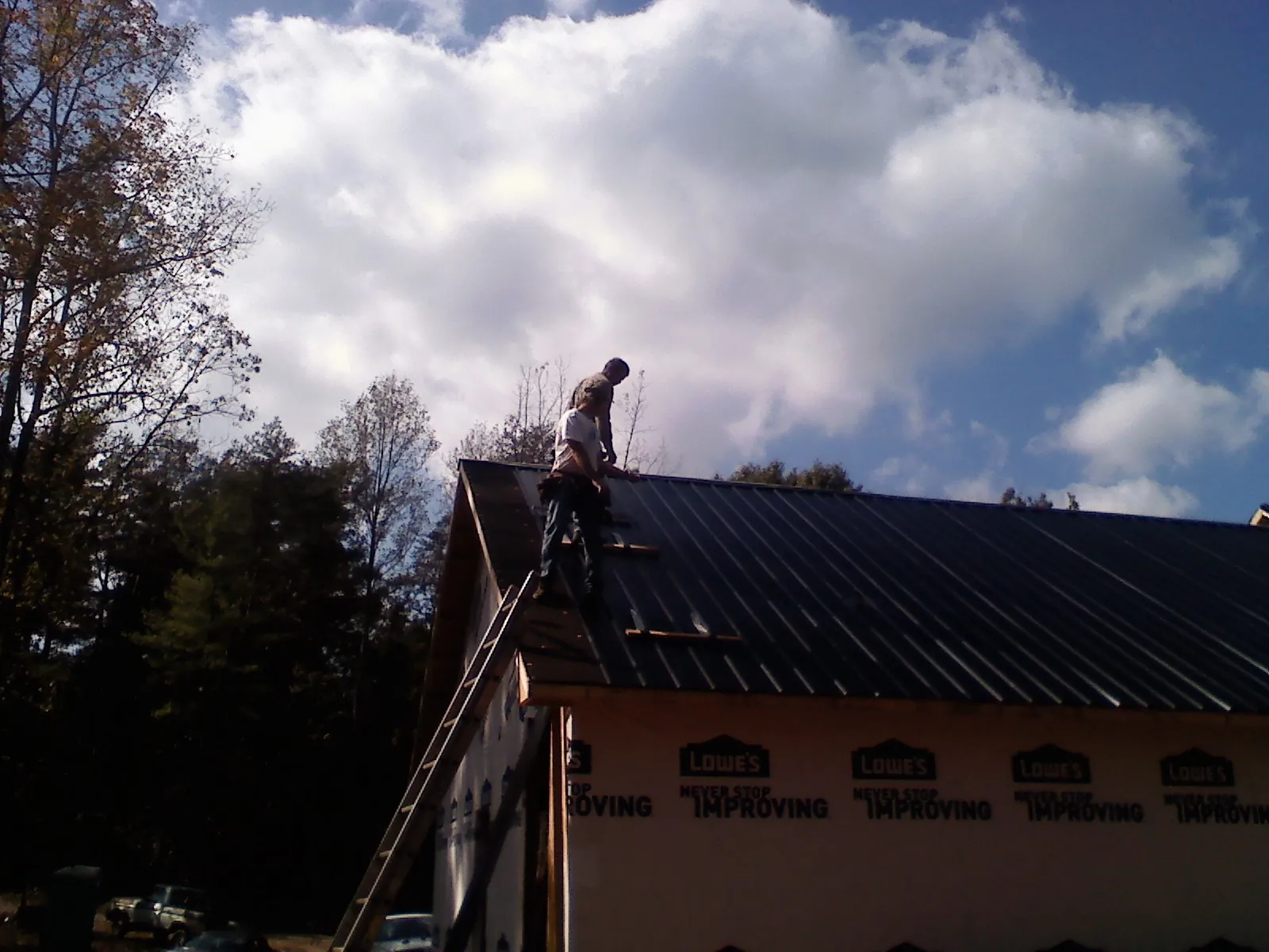 Roofer fastening dark metal panels high against a cloudy sky, from a Roof Inspection job in Echo